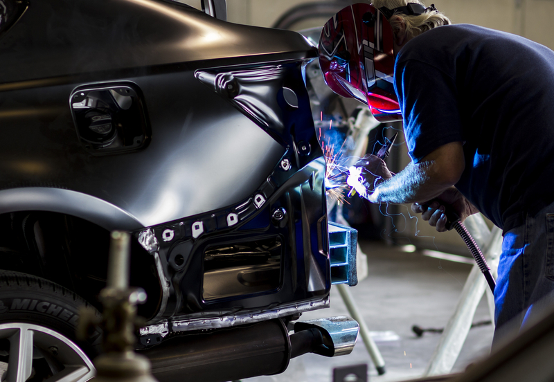 Auto body technician welding a black vehicle back end.