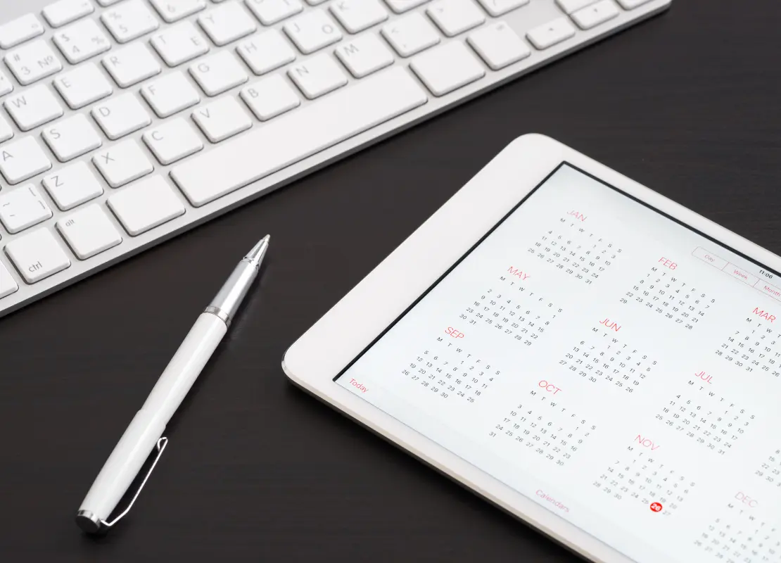 tablet showing yearly calendar, sitting next to white keyboard