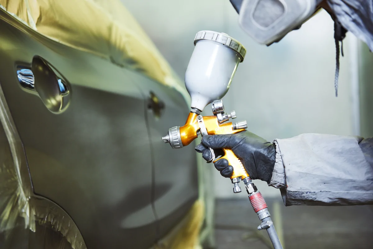 Auto paint refinishing technician spraying vehicle panel in Lewisville TX