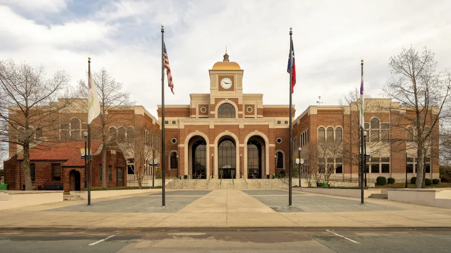 Front view of Lewisville City Hall in Lewisville, TX, featuring a clock tower, brick architecture, and surrounding flagpoles.